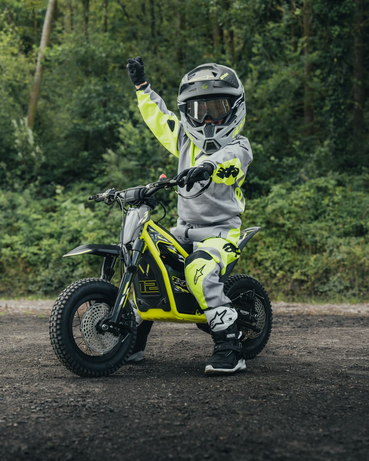 Child in motocross gear standing next to a electric bike in a forest setting